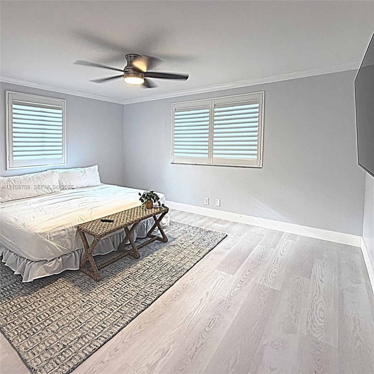 Wood-finish flooring, multi-pane windows with integrated shutters, neutral wall paint, and a ceiling-mounted light fixture with a fan