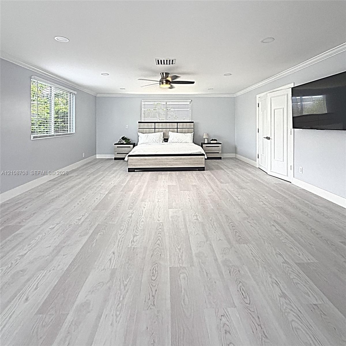 Spacious interior room featuring wood-finish flooring, recessed lighting, crown molding, a ceiling fan, and double panel doors