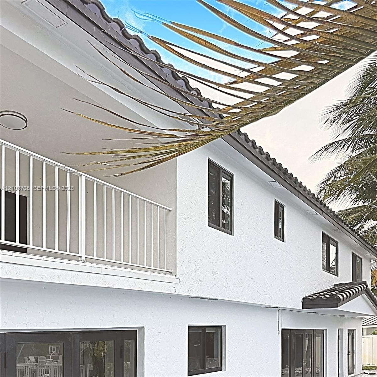 Exterior elevation featuring a stucco facade, dark-frame windows, a tiled roofline, and a covered balcony with a white metal railing