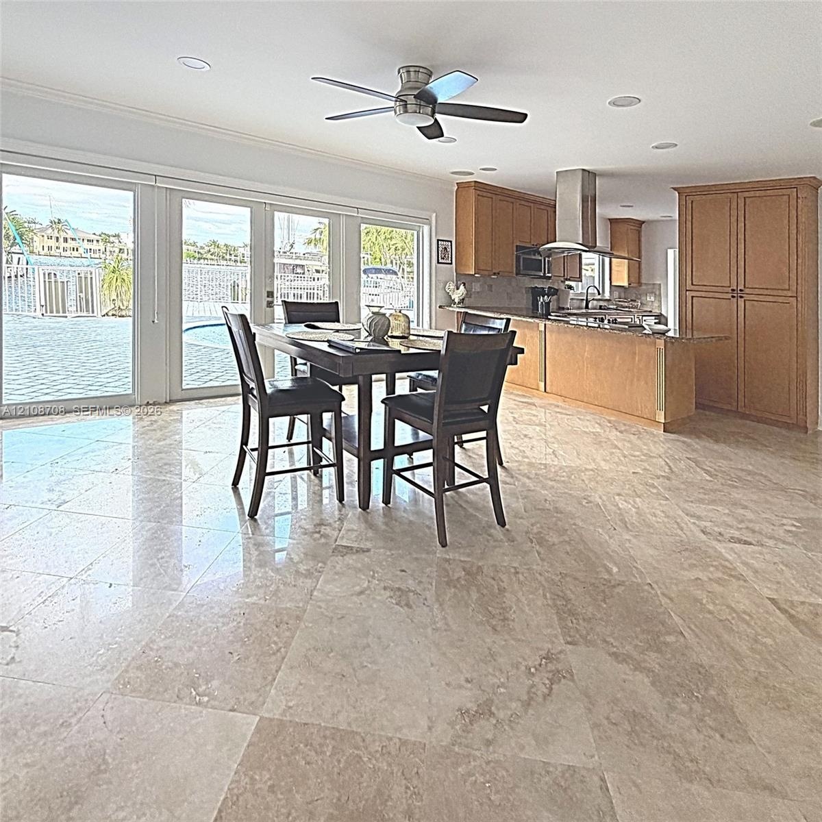Large-format stone tile flooring, wooden cabinetry, stainless steel range hood, recessed lighting, and expansive glass paneled doors