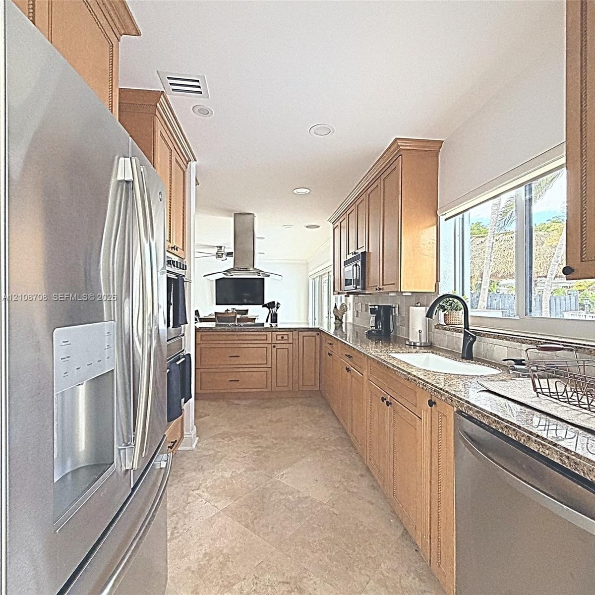 Kitchen featuring natural wood cabinetry, stone-finish countertops, stainless steel appliances, a center island with a chimney-style range hood, and t