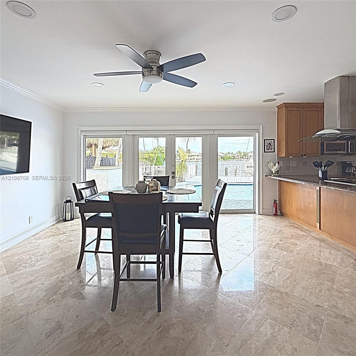 Open-concept interior featuring large-format stone tile flooring, stainless steel range hood, recessed lighting, ceiling fan, and multi-panel glass do