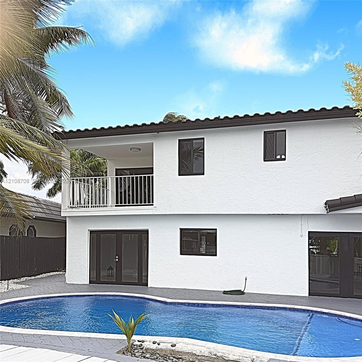 Stucco exterior featuring an upper-level balcony with white railings, a concrete pool deck, and a private swimming pool with tile finish