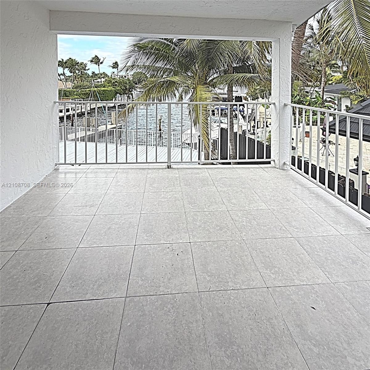 Covered balcony featuring large-format stone tile flooring and white metal railing, overlooking a canal with boat docking