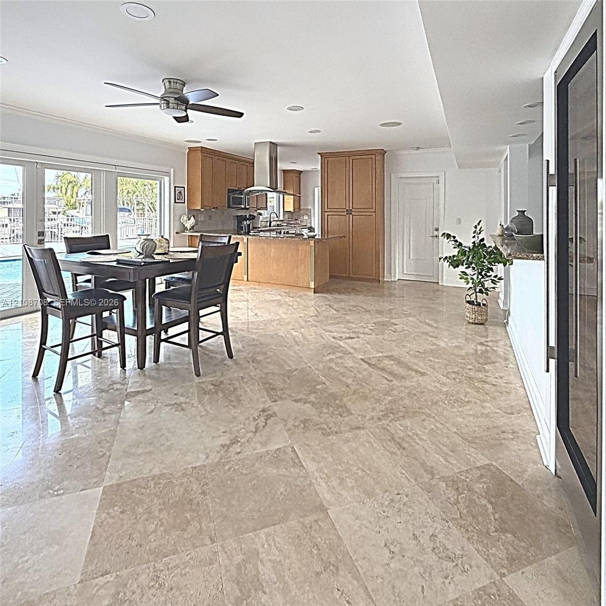 Open-concept kitchen featuring natural stone tile flooring, wood cabinetry, a stainless steel range hood, recessed lighting, and glass-paneled sliding