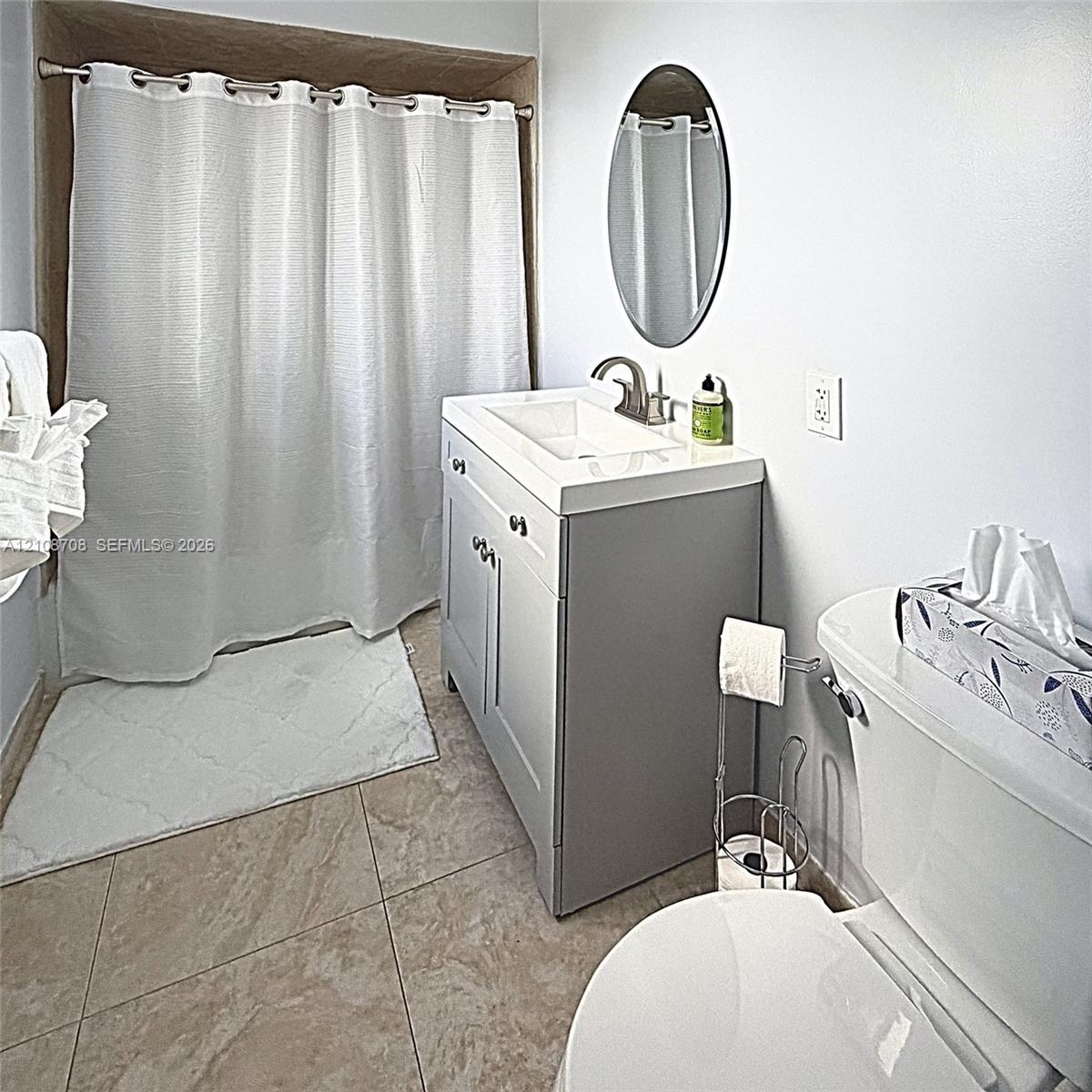 Bathroom featuring a vanity with a rectangular sink, oval wall-mounted mirror, ceramic tile flooring, and a tub-shower combination with a curtain rod