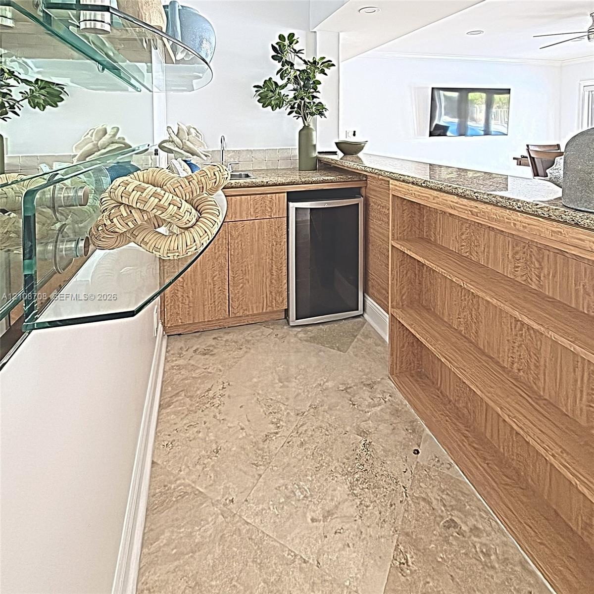 Wet bar featuring stone-finish countertops, light-toned wood cabinetry, built-in shelving, integrated beverage refrigerator, and stone tile flooring