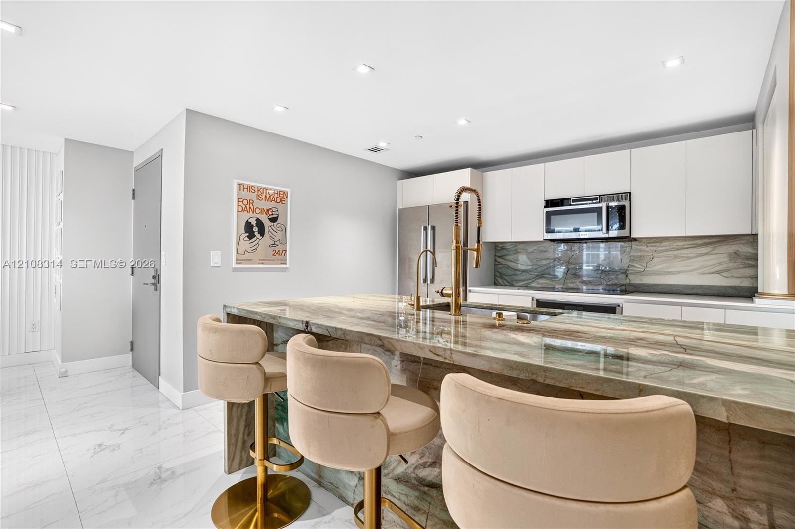 Kitchen featuring a stone waterfall island with a metal gooseneck faucet, white flat-panel cabinetry, a matching stone backsplash, stainless steel app