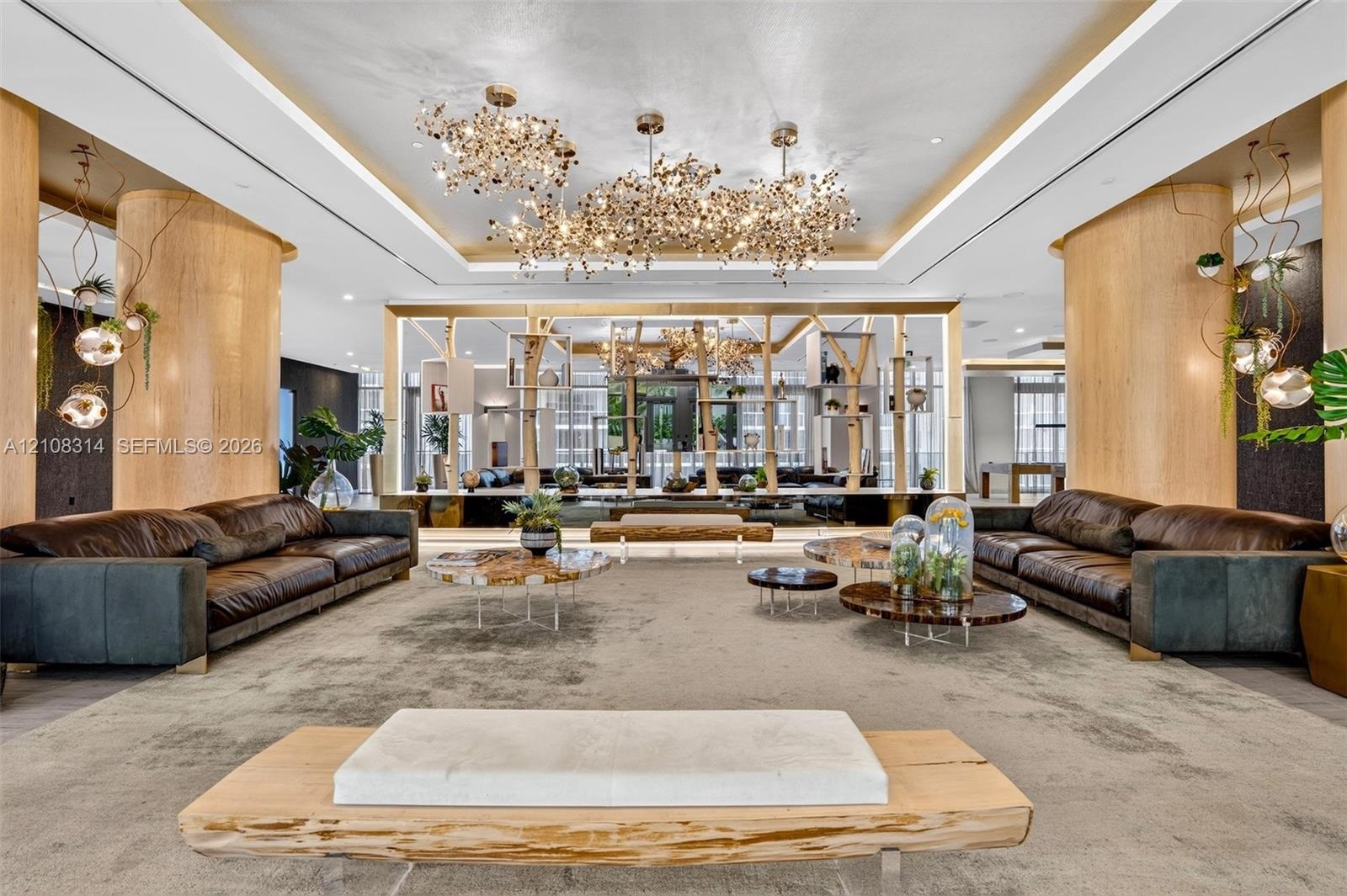 Expansive room featuring cylindrical wood-finished support columns, custom multi-cluster decorative chandeliers, recessed tray ceiling lighting, and a