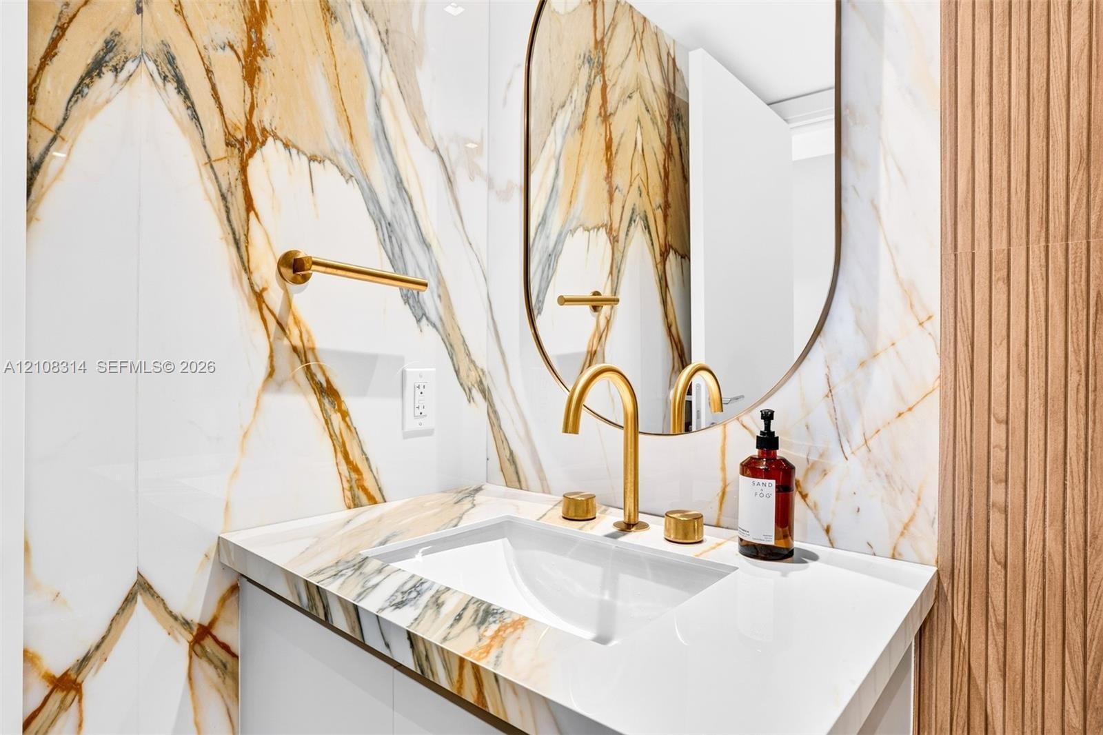 Wall-mounted vanity featuring large-format stone-patterned tile wall cladding, an integrated undermount sink, brass-finish widespread faucet, arched v