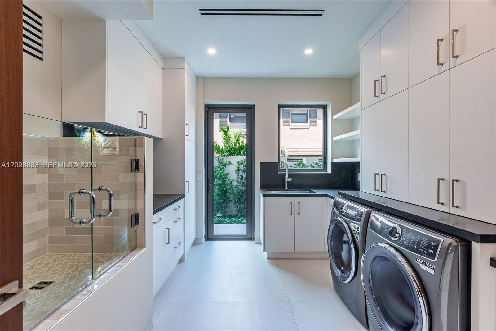 Utility room featuring extensive white cabinetry, dark solid-surface countertops, a deep undermount sink, porcelain tile flooring, and an enclosed til