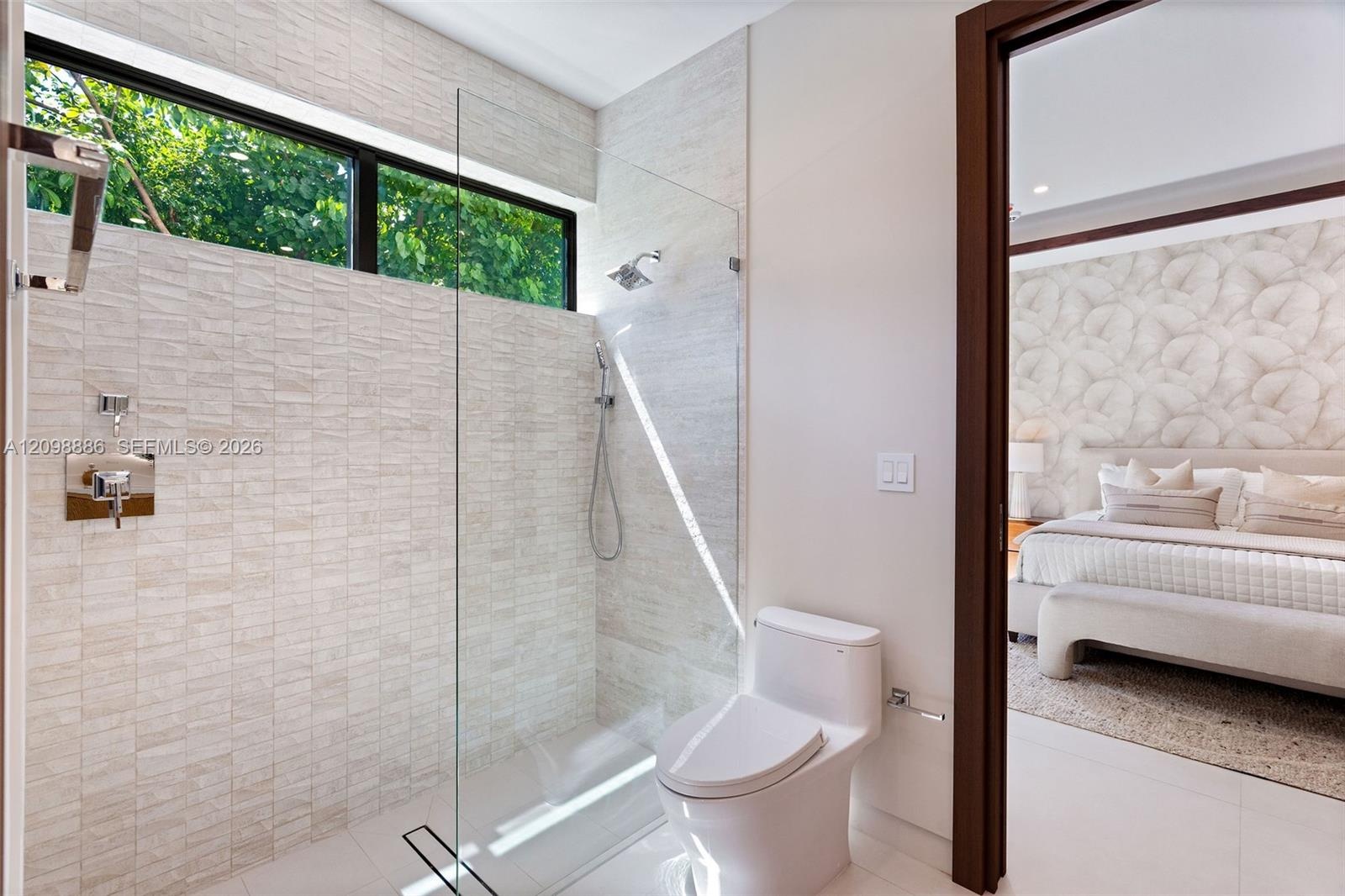 Walk-in shower featuring textured stone tile walls, a frameless glass panel, a rainfall showerhead, and a rectangular window, complemented by a one-pi