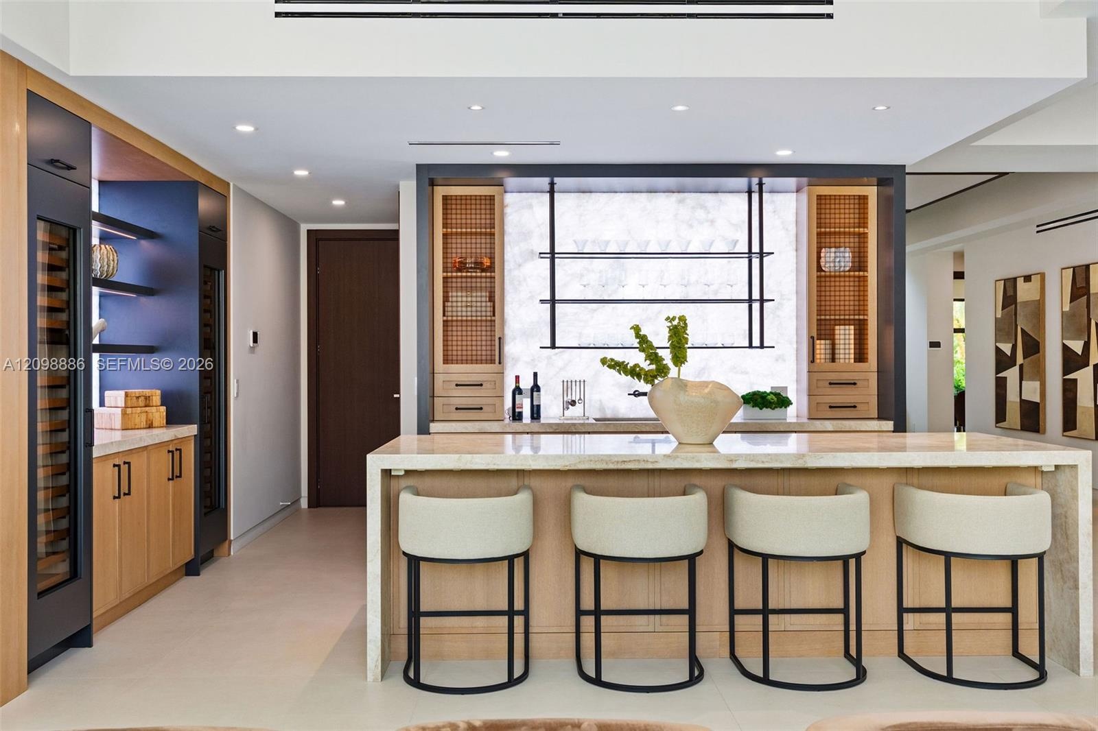 Custom bar area featuring stone slab backsplash, integrated wine refrigeration, built-in light wood cabinetry, stone-topped island with waterfall edge