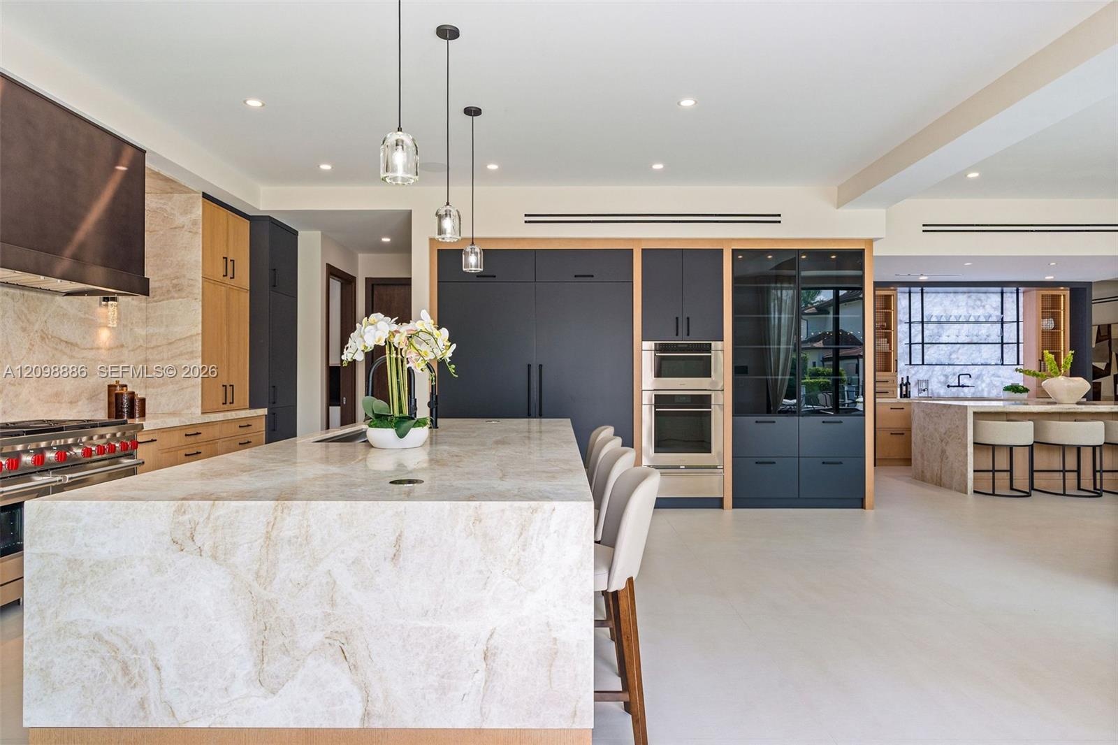 Kitchen featuring a waterfall-edge island with stone surfacing, stainless steel double wall ovens, paneled cabinetry, glass-front display shelving, an