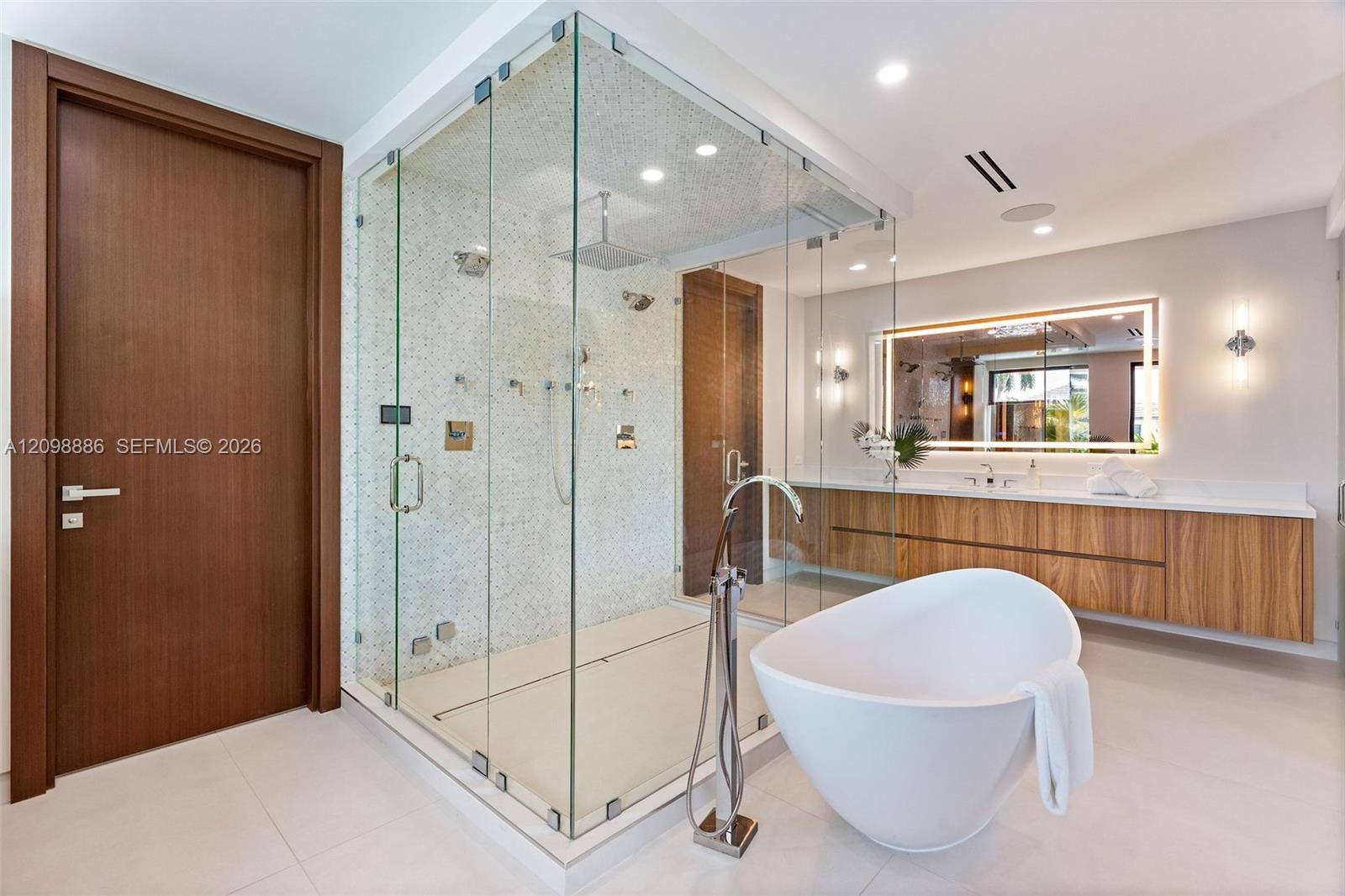 Glass-enclosed walk-in shower with mosaic tile surround and rainfall showerhead, freestanding soaking tub with floor-mounted faucet, wall-mounted wood