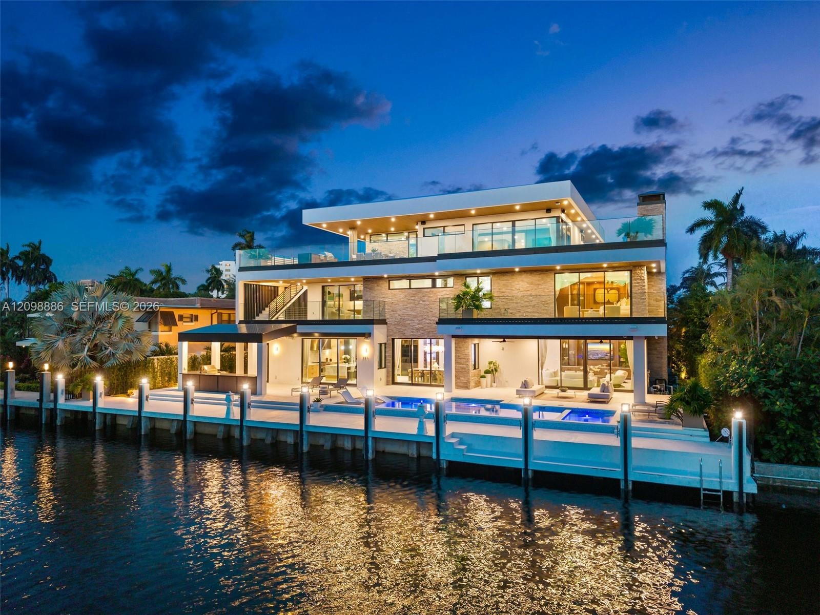Multi-story modern residence featuring stone veneer siding, expansive glass sliders, multiple tiered balconies with glass railings, a swimming pool, a
