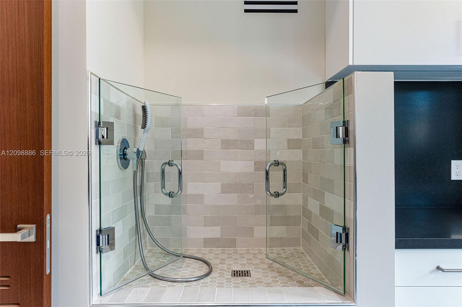 Glass-enclosed station featuring a handheld shower fixture, subway-tile wall surround, hexagonal floor tile, and polished chrome hardware