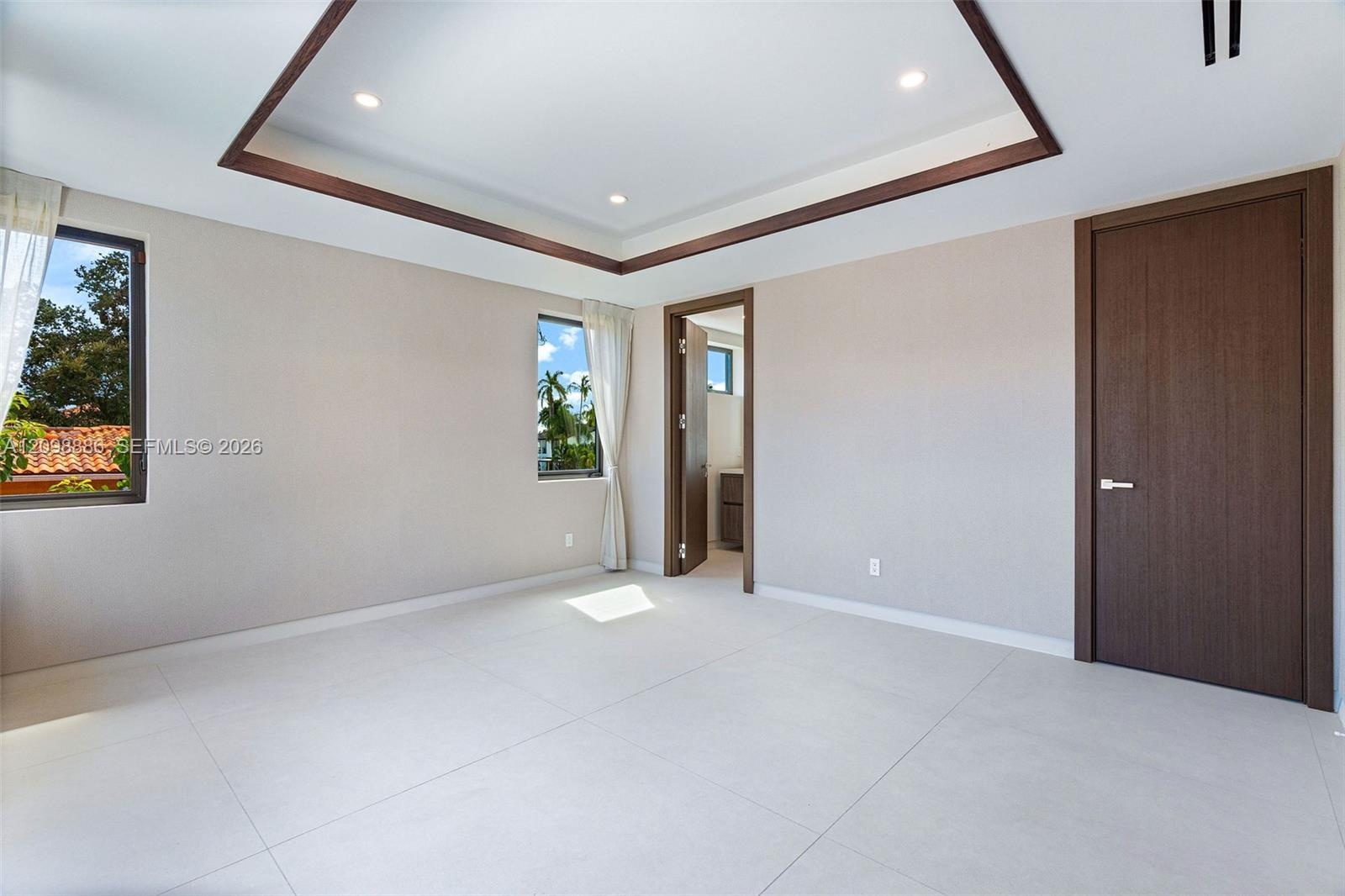 Tray ceiling with dark wood-finish trim, recessed lighting, large-format tile flooring, and solid core doors