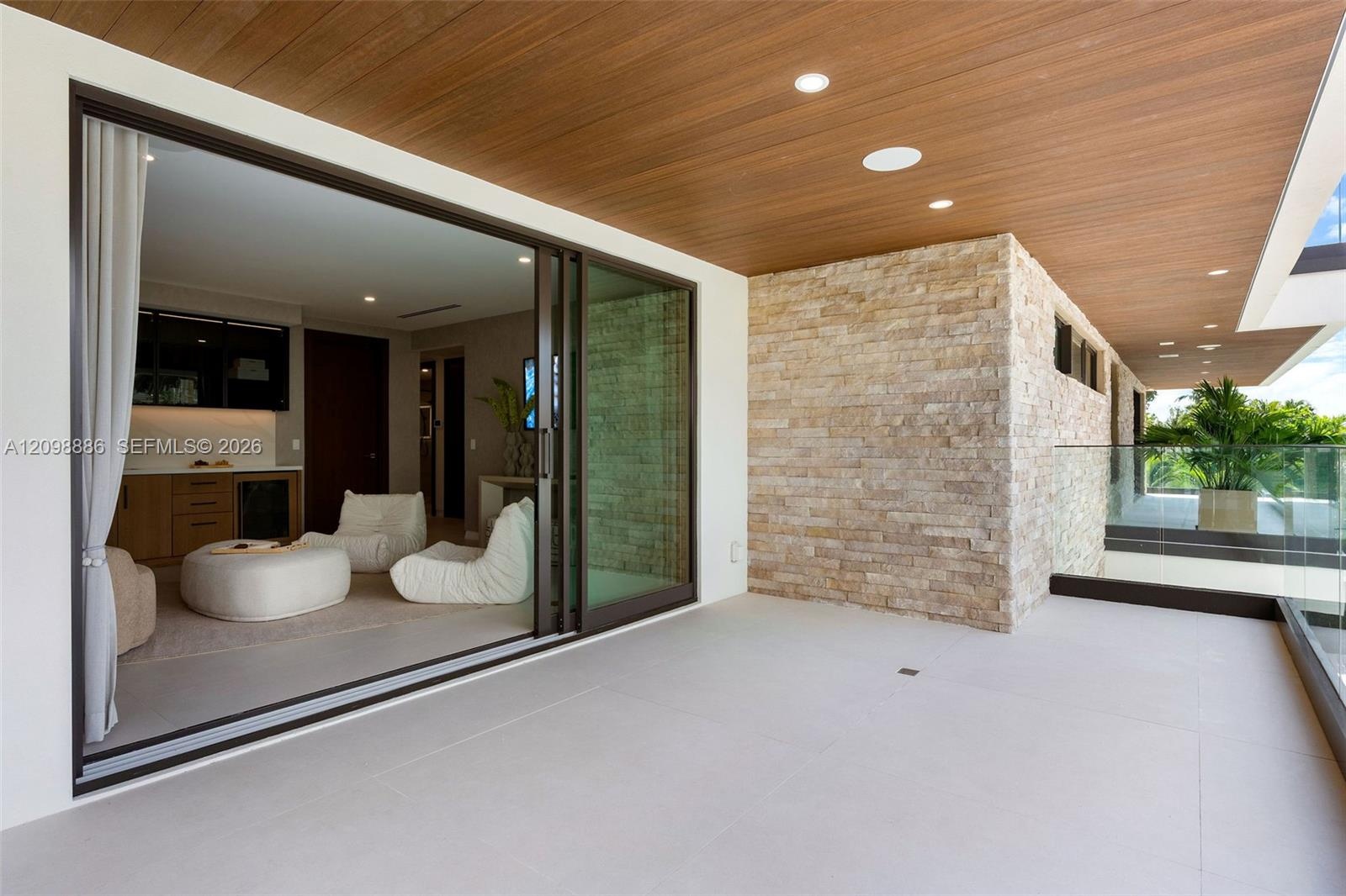 Covered balcony featuring wood-plank ceiling, large-format tile flooring, stacked-stone accent wall, recessed lighting, and expansive glass sliding do