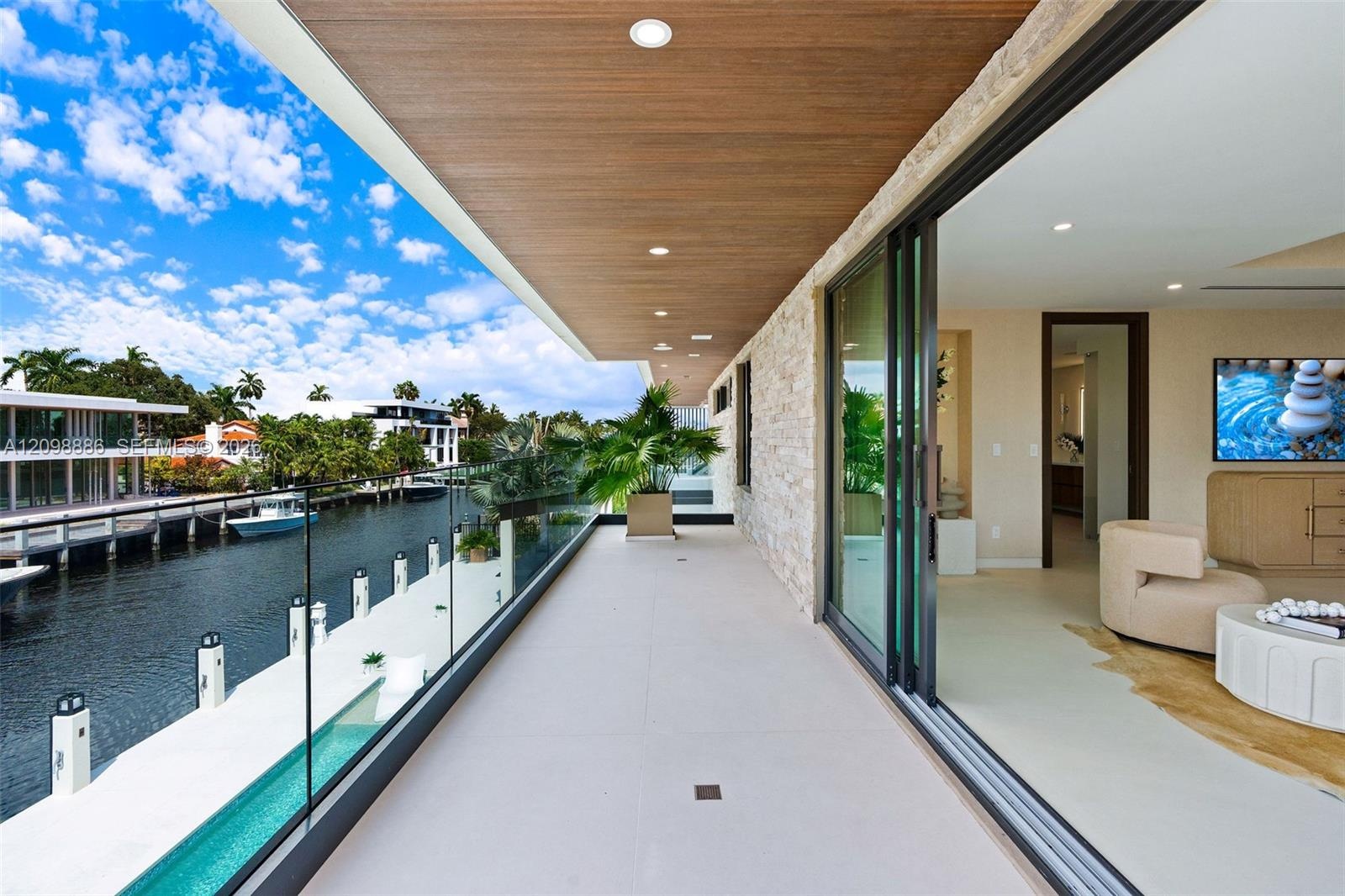 Covered balcony featuring recessed lighting, a wood-finish ceiling, natural stone wall cladding, a glass panel railing, and large-format tile flooring