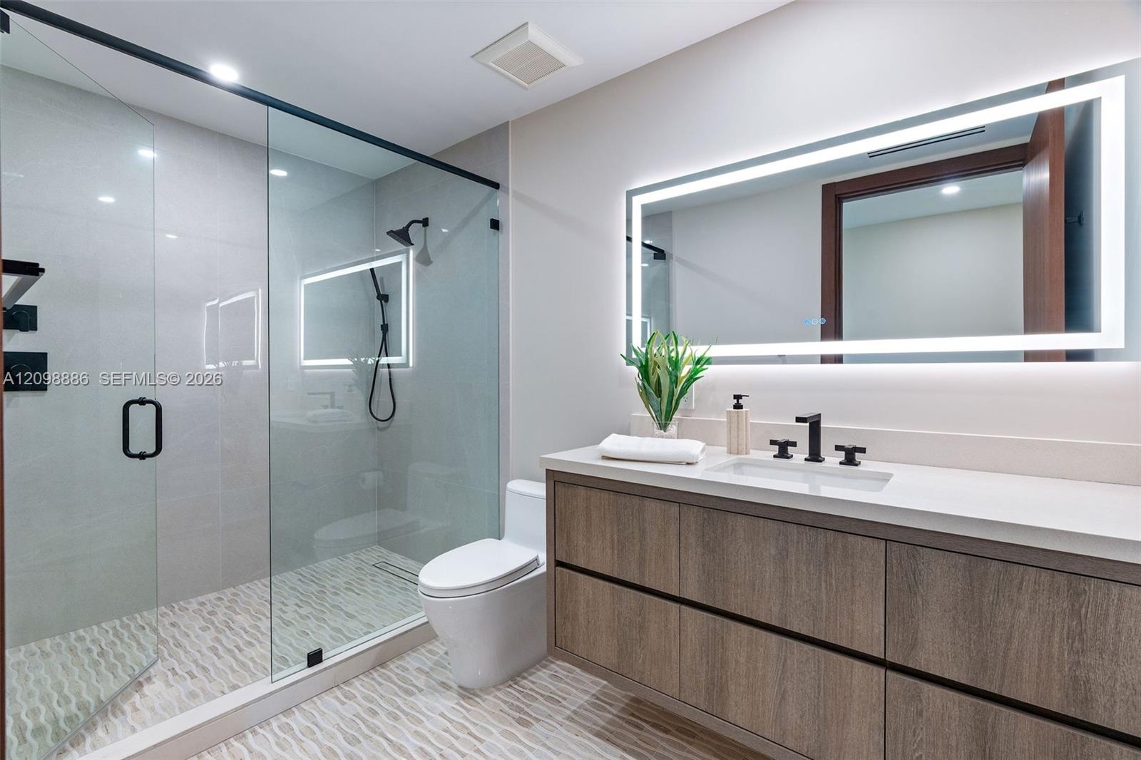 Modern bathroom featuring a wood-finish floating vanity with a white countertop, walk-in glass-enclosed shower with matte black fixtures, and a large 