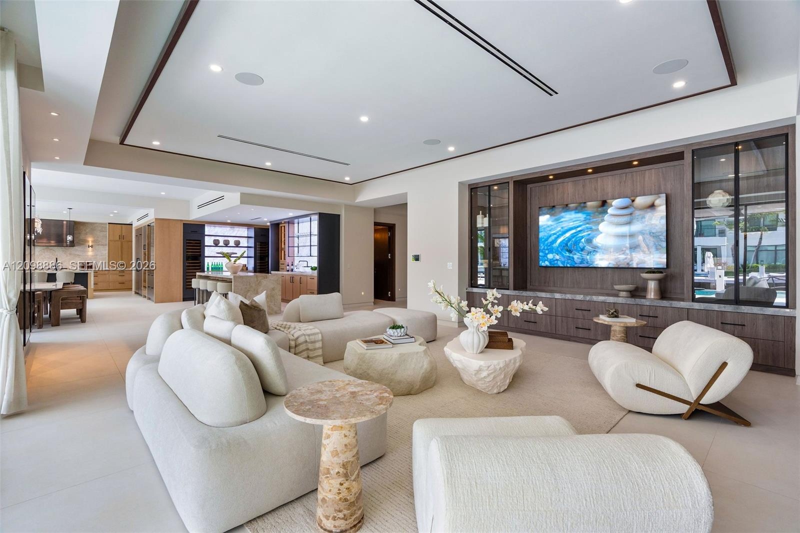Open-concept living space featuring a recessed tray ceiling, custom built-in cabinetry with integrated display lighting, and large-format tile floorin