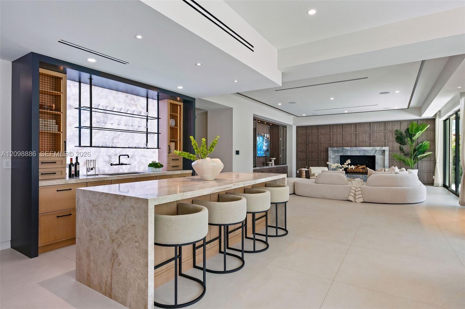 Stone-topped kitchen island with bar seating, custom cabinetry featuring integrated shelving, recessed lighting, and floor-to-ceiling wood wall paneli