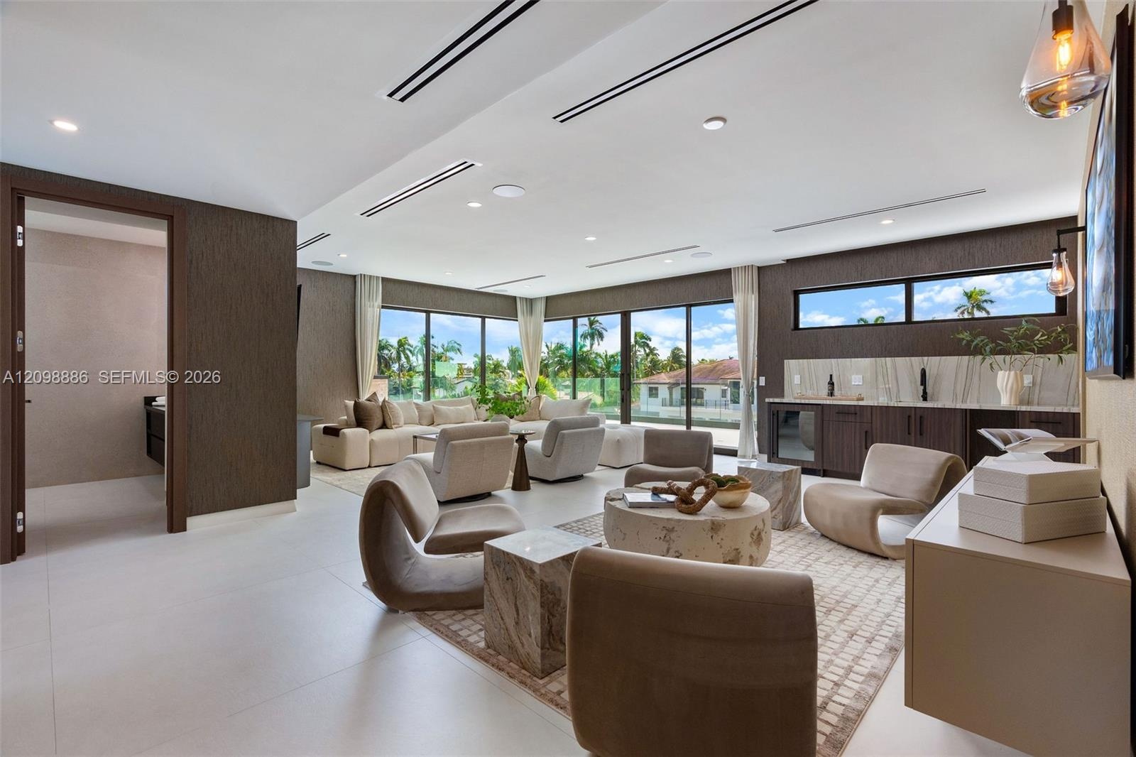 Large-format tile flooring, recessed linear lighting, floor-to-ceiling glass sliding doors, built-in wet bar with stone backsplash, and dark textured 