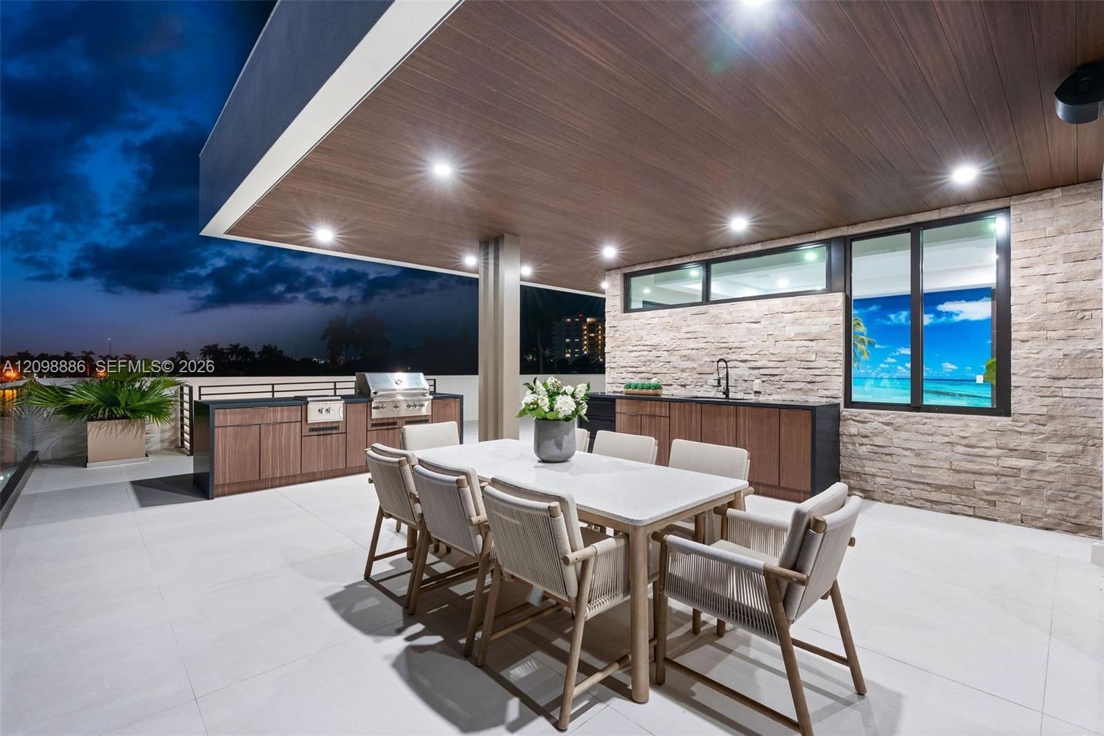Covered outdoor terrace featuring a built-in stainless steel grill, stone veneer accent wall, recessed lighting, and expansive wood-finish ceiling sof