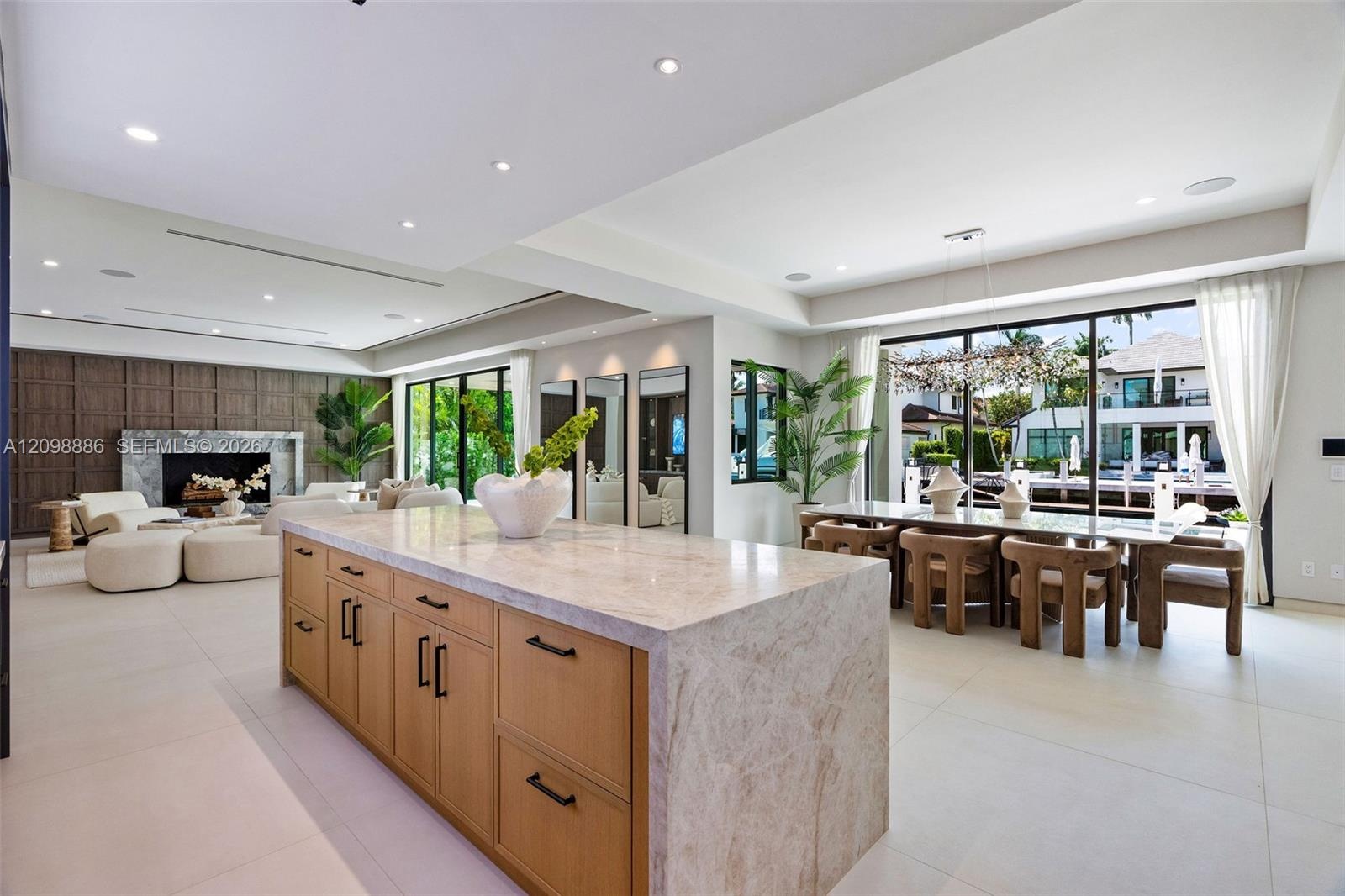 Large kitchen island featuring a waterfall stone countertop and light wood-finish cabinetry with matte black hardware, stone tile flooring, a floor-to