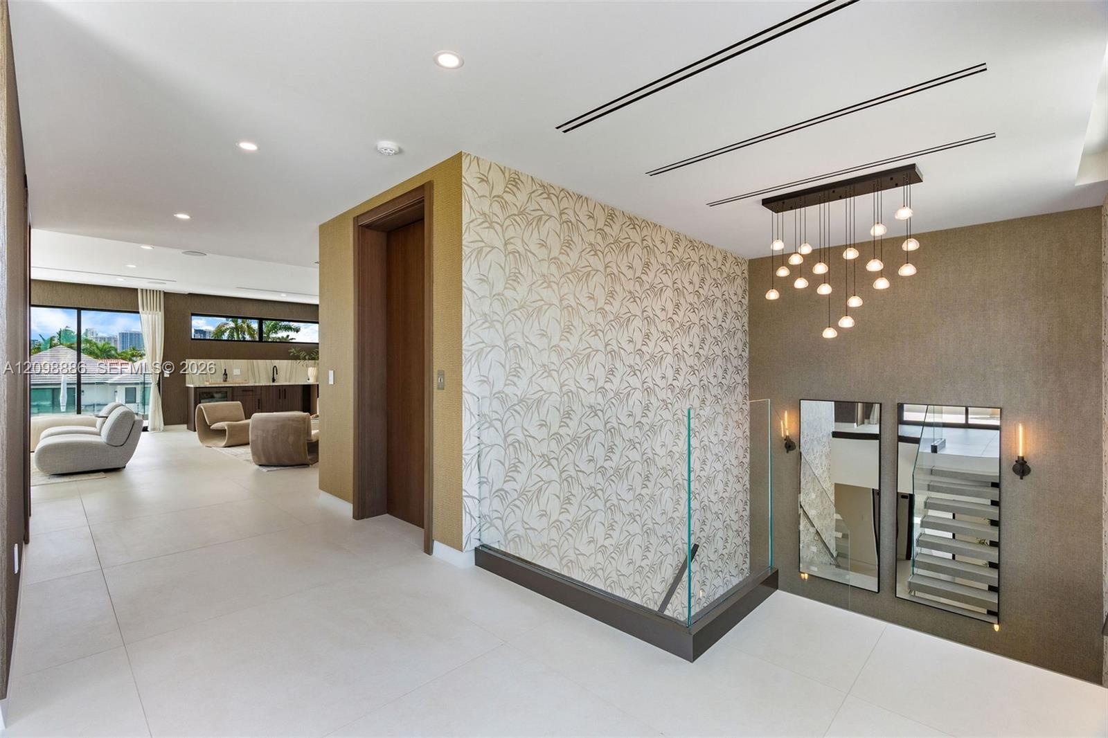 Interior space featuring large-format tile flooring, patterned accent wall, glass panel railing, multi-pendant chandelier, and recessed linear lightin