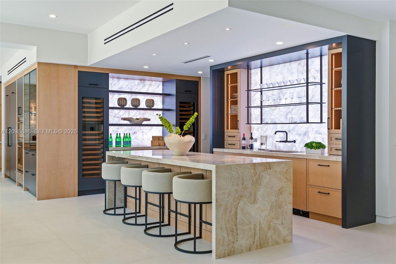 Kitchen featuring a waterfall-edge stone island, built-in dual wine refrigeration, stone slab backsplash, recessed ceiling lighting, and custom cabine