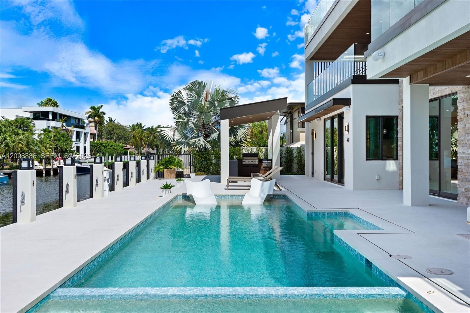 Waterfront outdoor living space featuring a custom swimming pool with a sun shelf, a covered patio area, and concrete decking