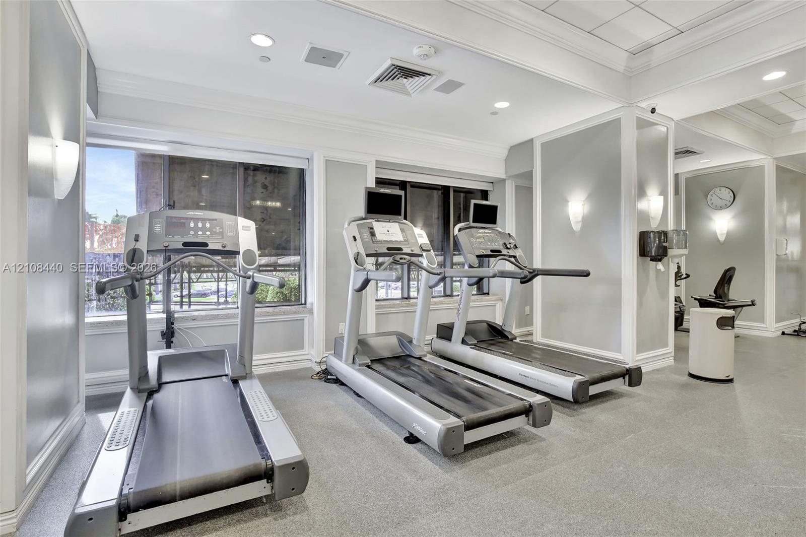 Fitness center featuring large windows, recessed ceiling lighting, wall-mounted sconces, and crown molding