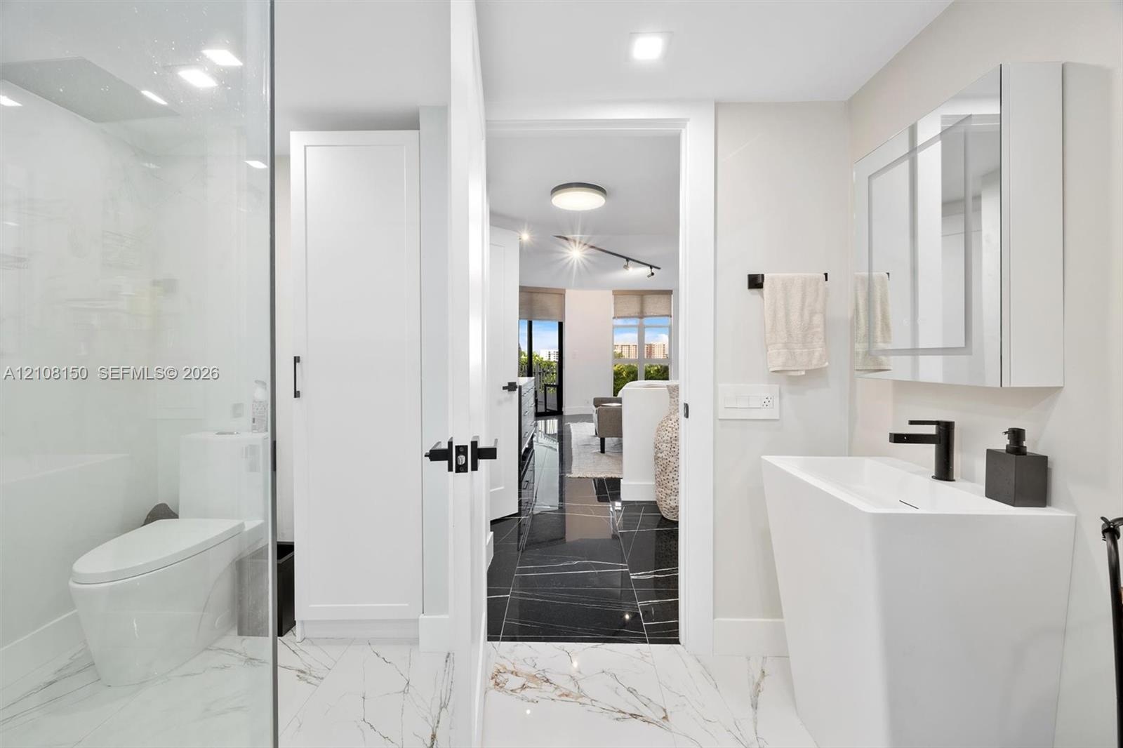 Modern bathroom featuring a tall white pedestal sink with matte black hardware, a glass-enclosed shower, built-in cabinetry, and white tile flooring w