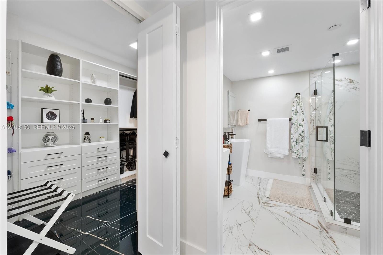 Walk-in closet featuring white built-in shelving and drawer cabinetry, complemented by high-gloss dark stone-finish flooring
