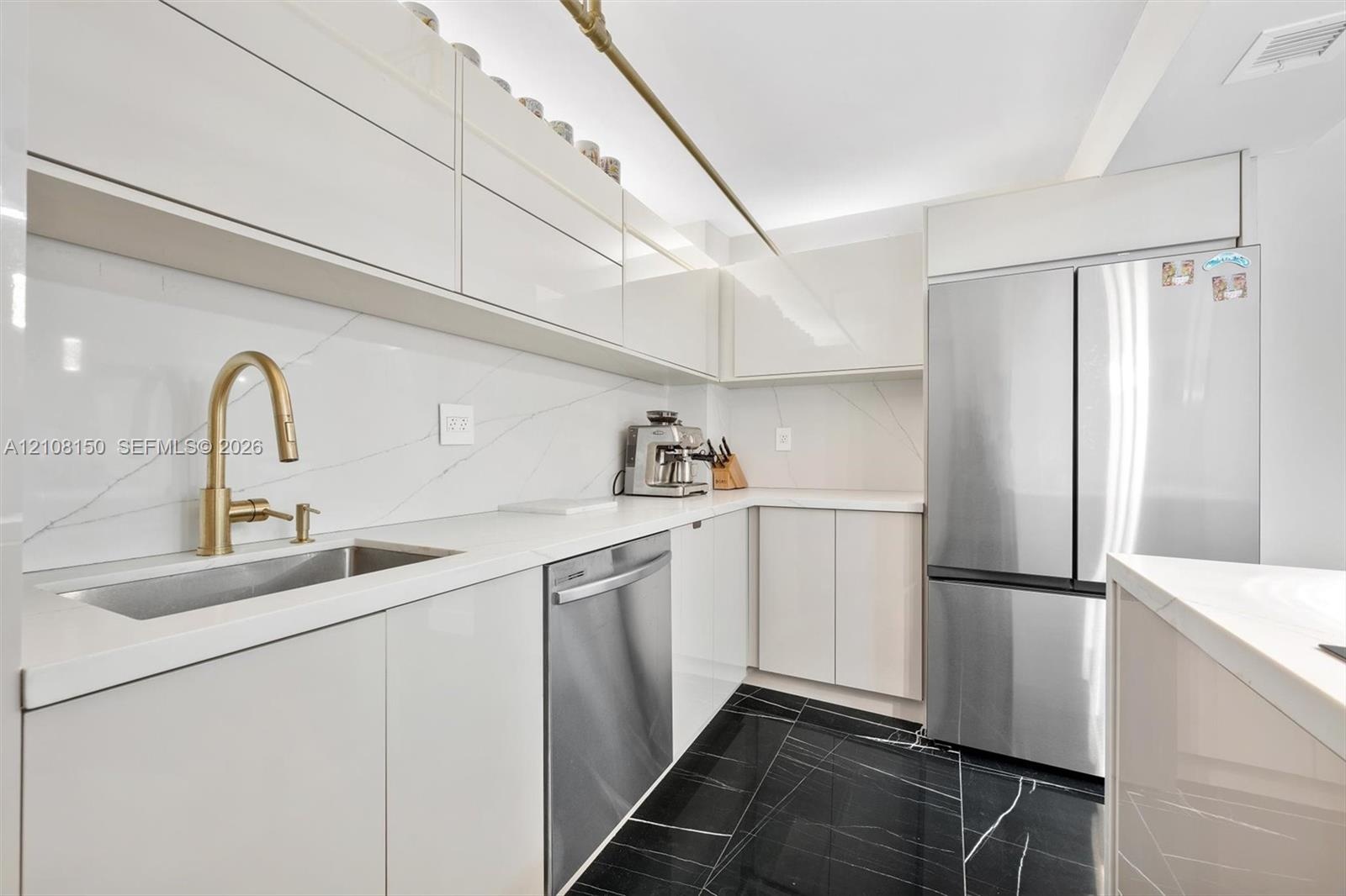 Kitchen featuring high-gloss cabinetry, stone-surface countertops, full-height stone backsplash, stainless steel appliances, and dark-toned flooring w