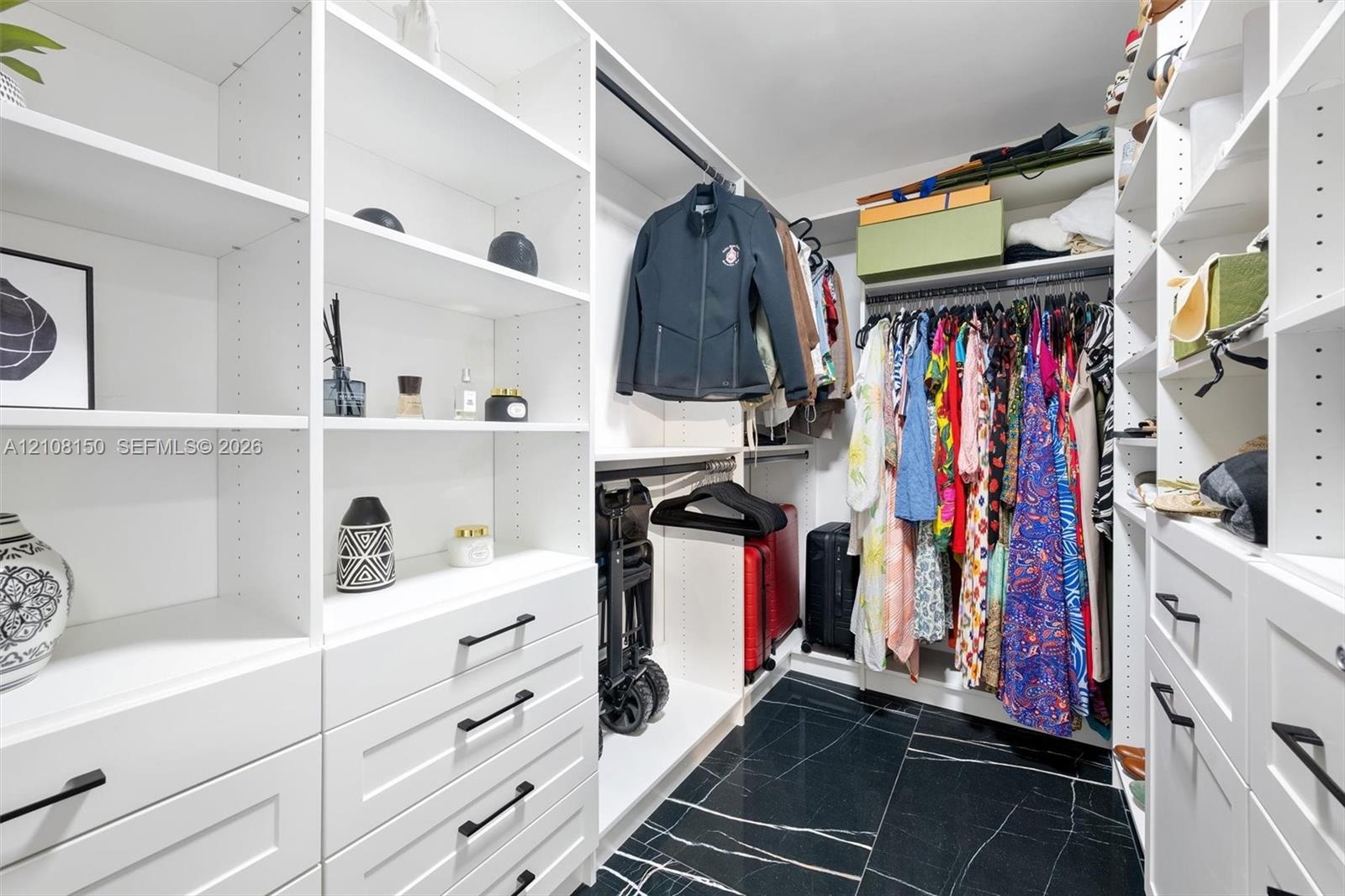 Custom walk-in closet featuring white built-in shelving, floor-to-ceiling storage units, multiple drawers with matte black hardware, integrated hangin
