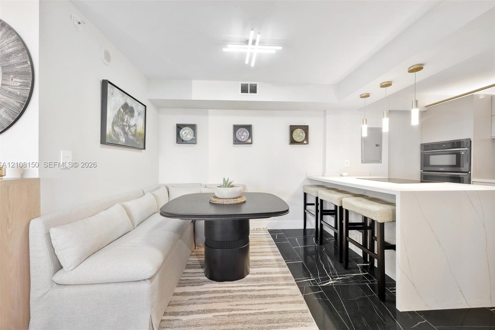 Kitchen featuring a stone-surface waterfall island, black tile flooring with white veining, built-in dual ovens, and trio of pendant lights