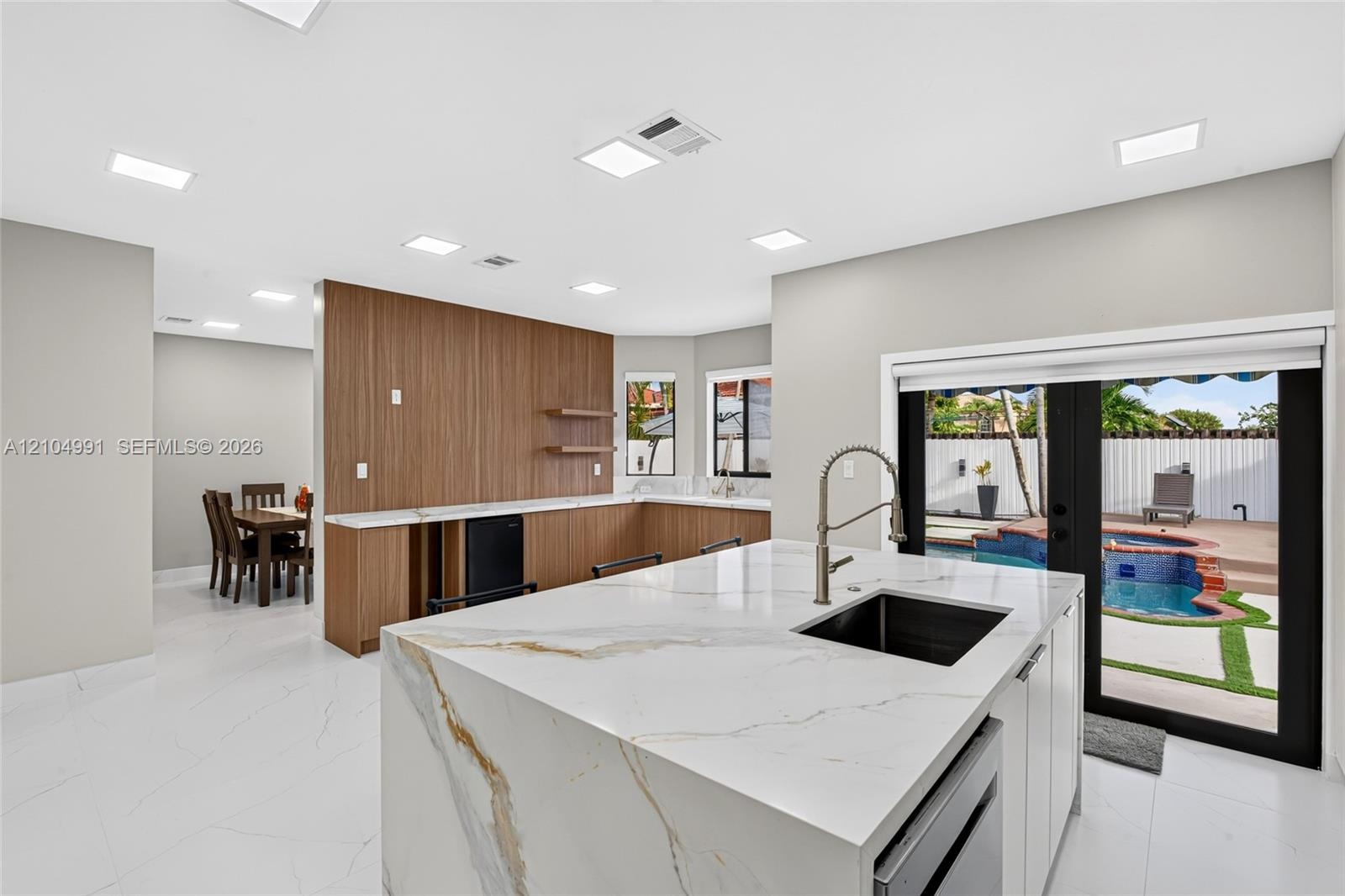 Kitchen featuring an island with a stone-finish countertop, undermount sink, matte black gooseneck faucet, wood-finish cabinetry, and recessed lightin