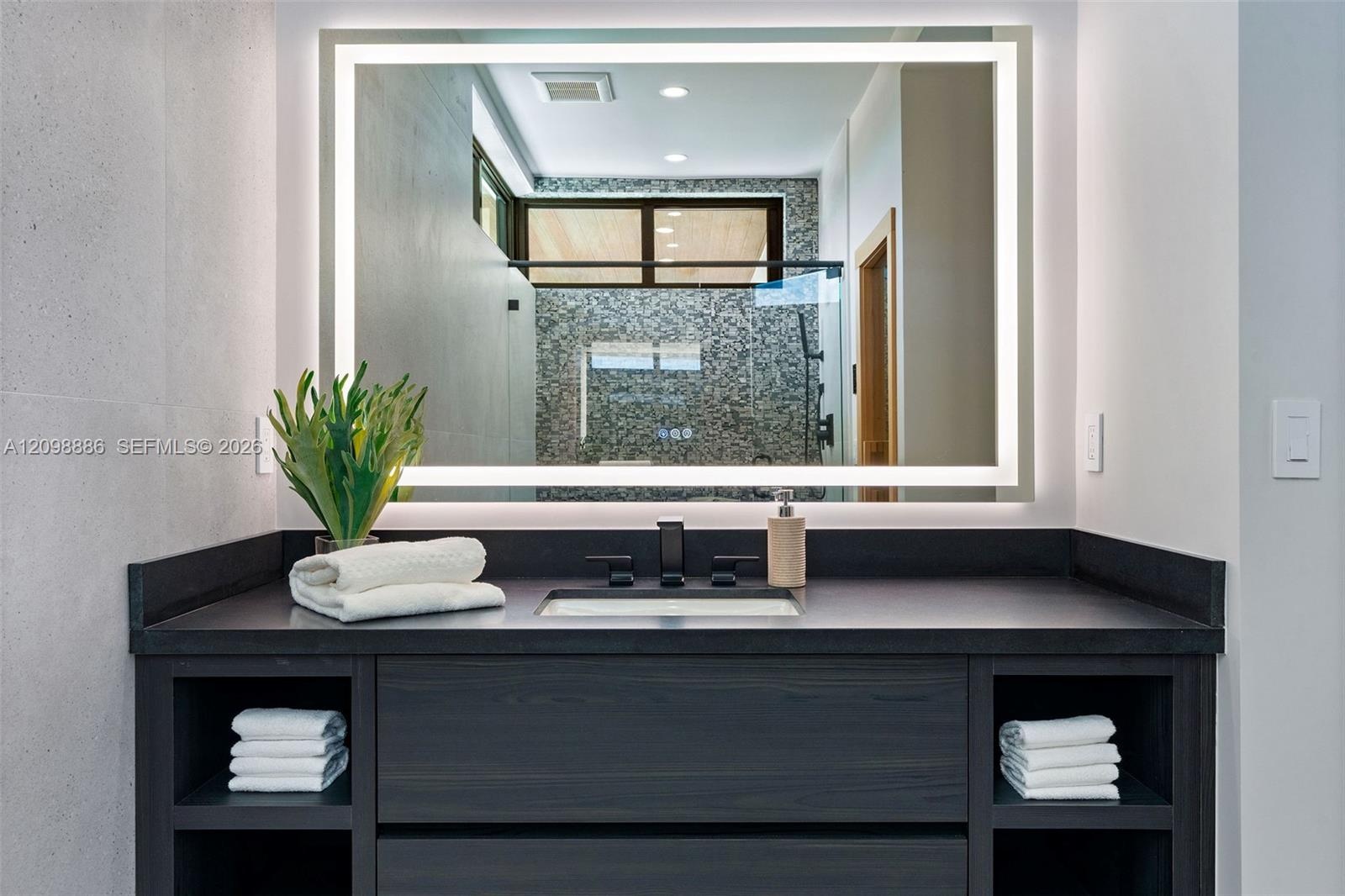 Dark wood vanity featuring integrated open shelving, a dark solid-surface countertop, an undermount rectangular sink, and a matte black faucet paired 