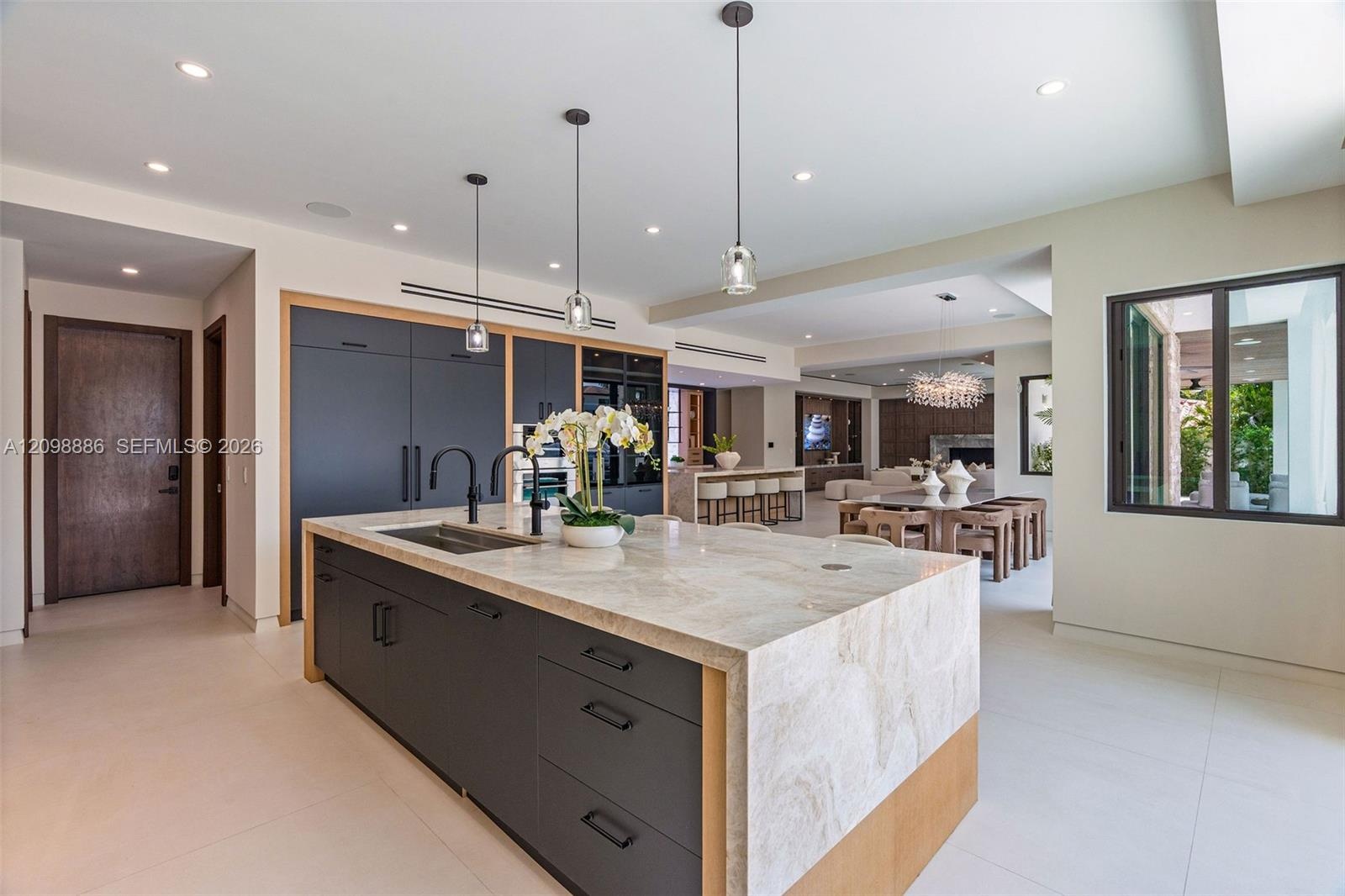 Kitchen featuring a waterfall-edge stone island, matte black hardware, integrated cabinetry, recessed lighting, and large-format tile flooring