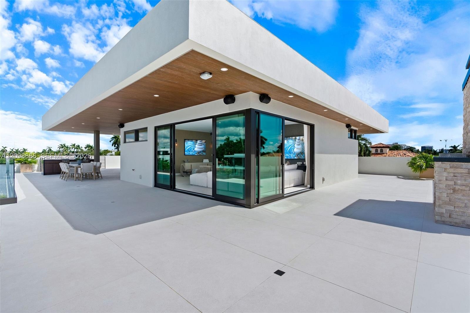 Expansive rooftop terrace featuring large-format tile flooring, a cantilevered roof overhang with wood-finish soffits, recessed lighting, and floor-to