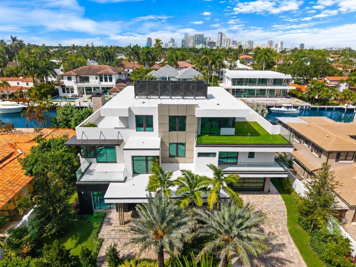 Multi-level contemporary residence featuring a flat roofline, glass panel balcony railings, stone-paved driveway, elevated terrace with turf surfacing