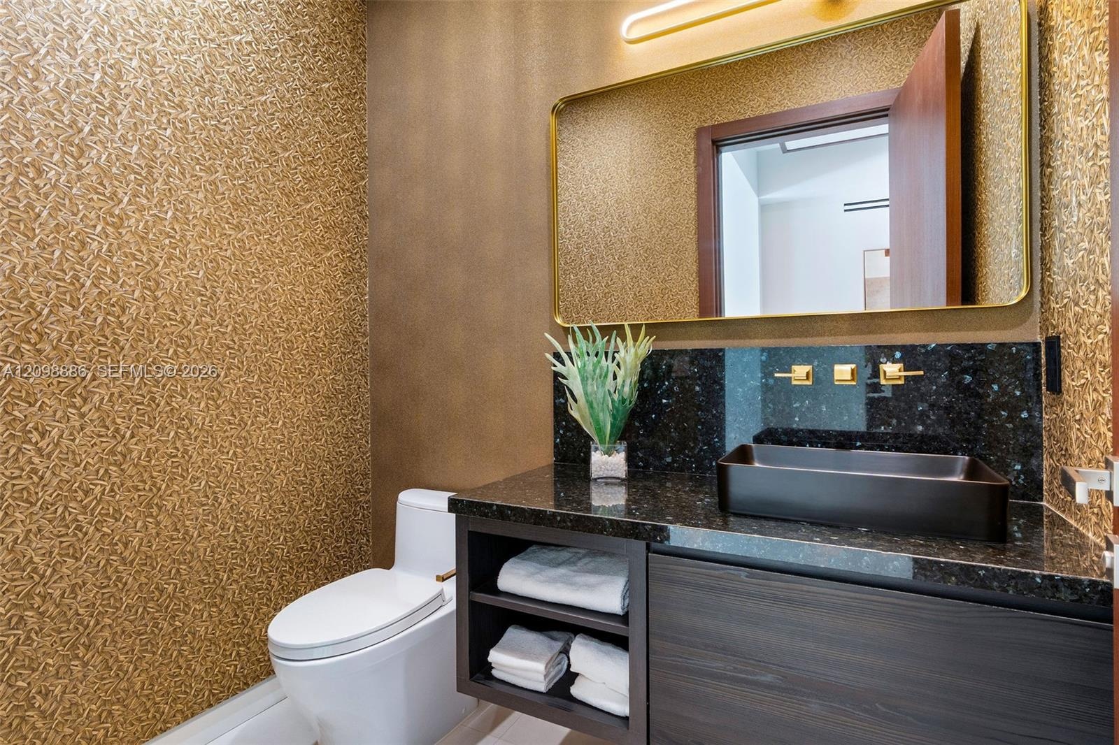 Floating vanity featuring a dark wood-finish, polished stone countertop, and rectangular vessel sink with gold-tone wall-mounted hardware