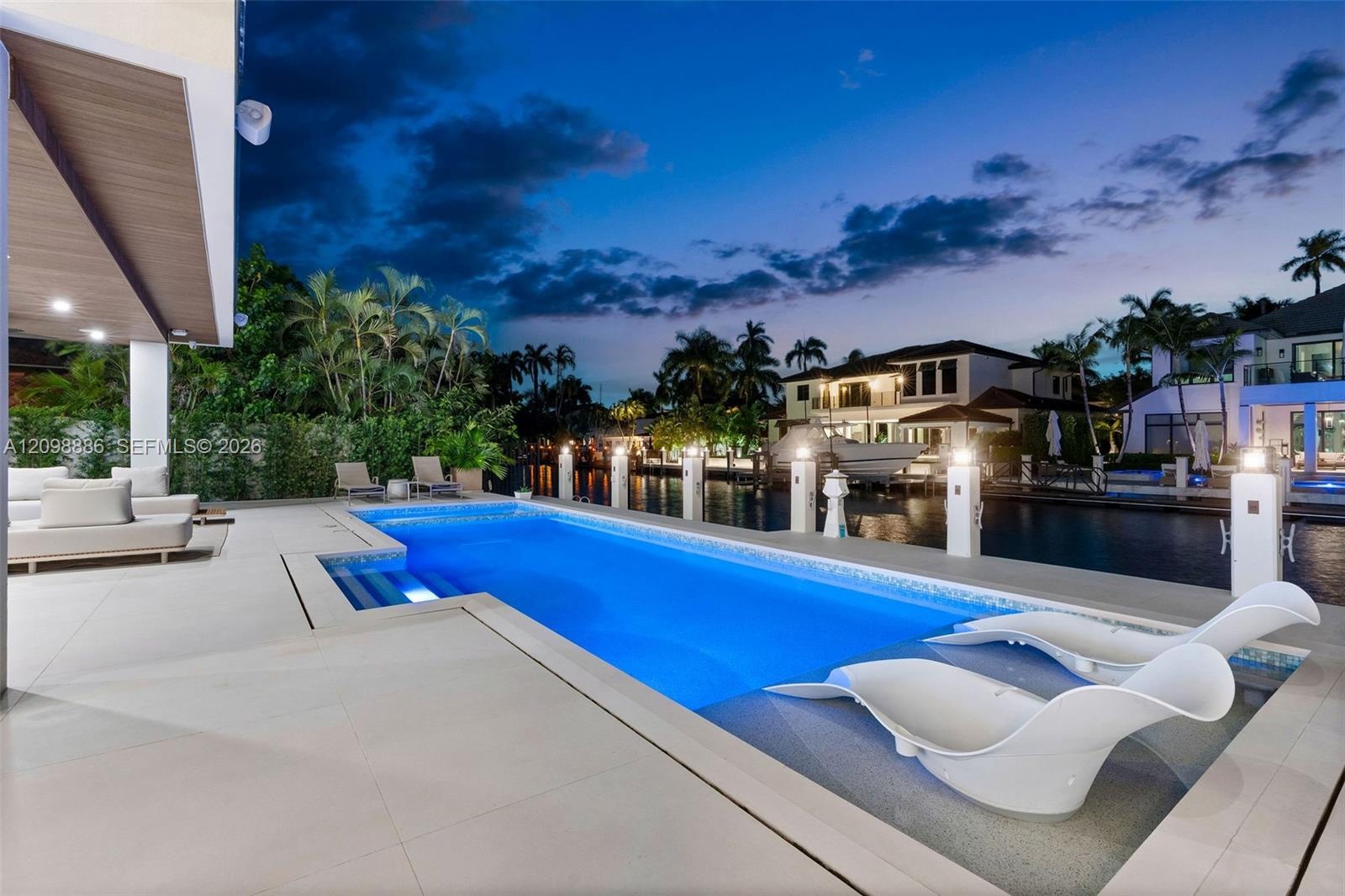 Rectangular swimming pool featuring a tanning ledge and tile surround, set against a waterfront bulkhead with concrete patio and recessed ceiling ligh