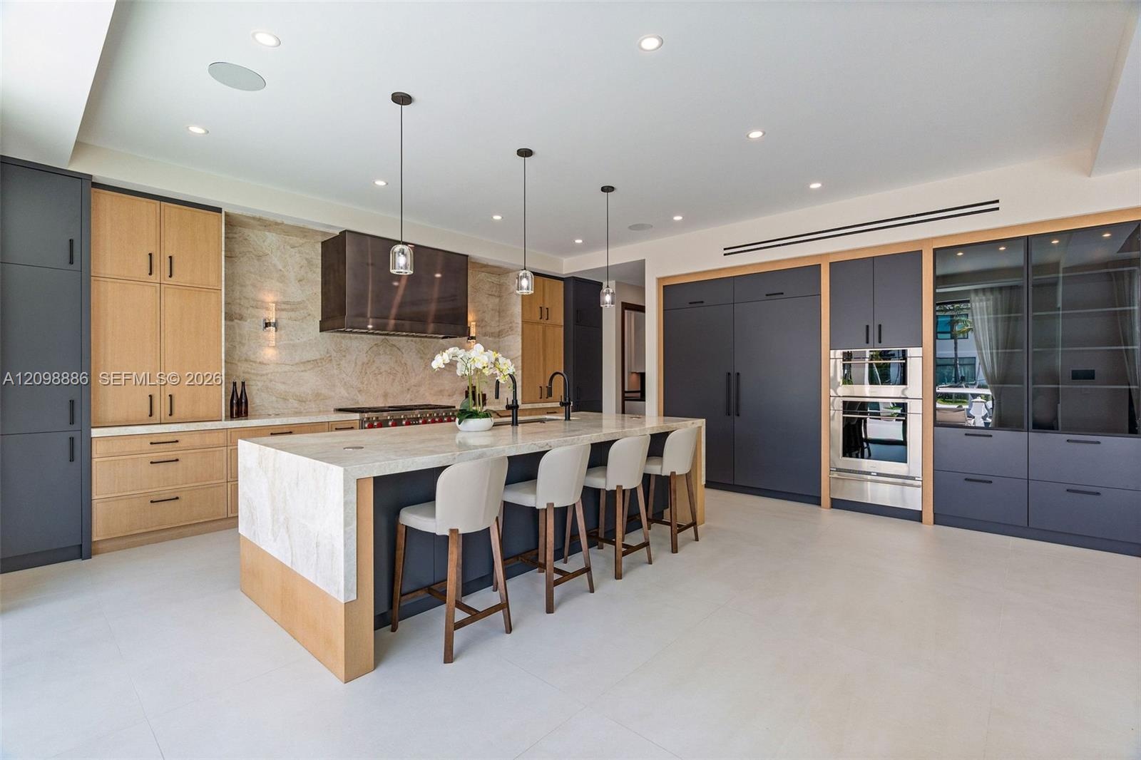 Kitchen featuring custom two-tone cabinetry, expansive stone-topped central island, built-in stainless steel double ovens, integrated refrigerator, an