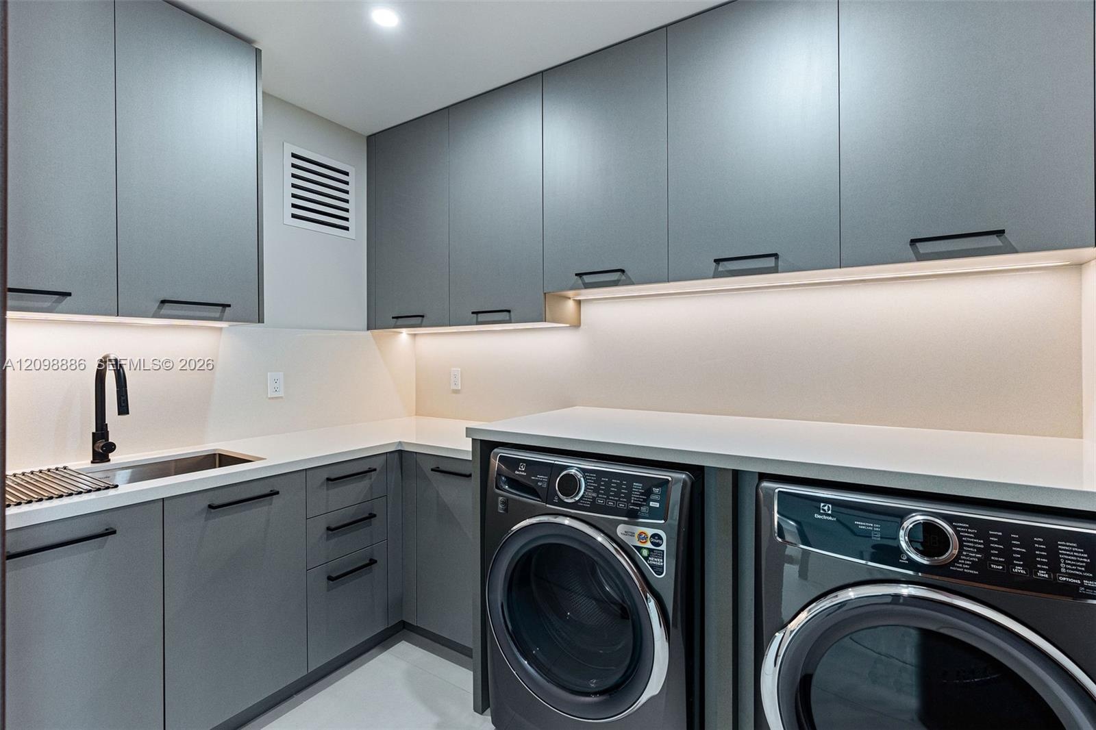 Modern cabinetry with matte hardware, light-toned countertop, undermount sink with a matte black faucet, and under-cabinet integrated lighting