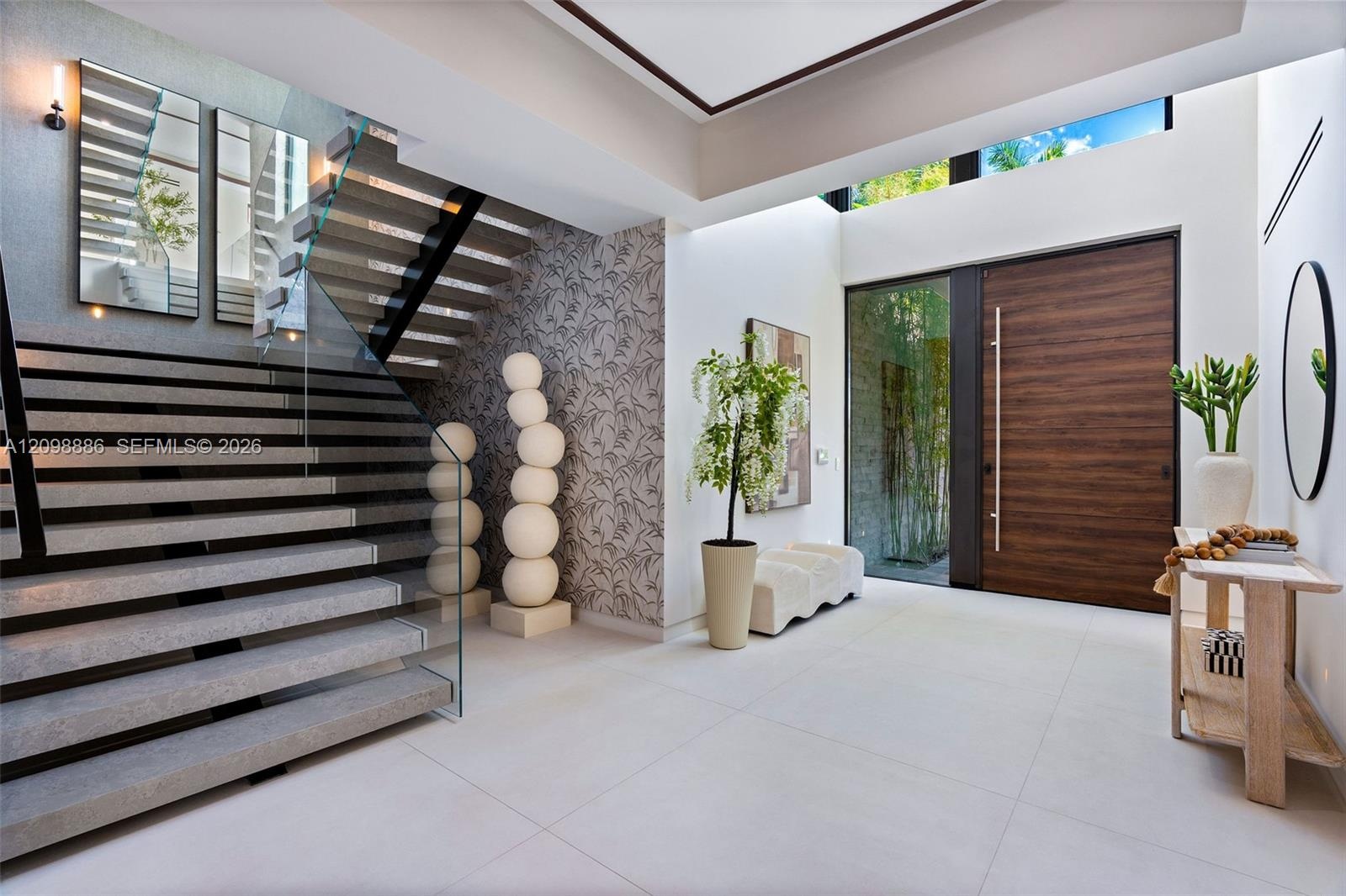 Grand foyer featuring large-format tile flooring, a custom wood-finished entry door with a vertical pull handle, a dramatic staircase with glass raili