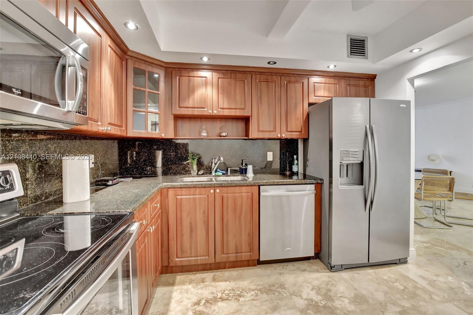 Kitchen featuring wood cabinetry, stone countertops, dark stone backsplash, stainless steel appliances, and recessed lighting
